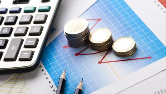 Calculadora, lápis e moedas em cima de gráficos