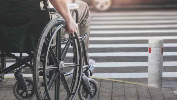 Disabled man on wheelchair preparing to cross the road on pedestrian crossing, copy space.